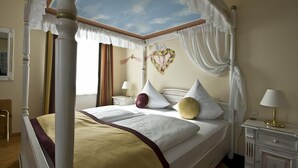 A four-poster canopy bed with a heart-shaped decoration on the wall, a bedside table with a lamp, and a window with curtains. - Hotel Restaurant Speeter (Weisenheim am Berg)