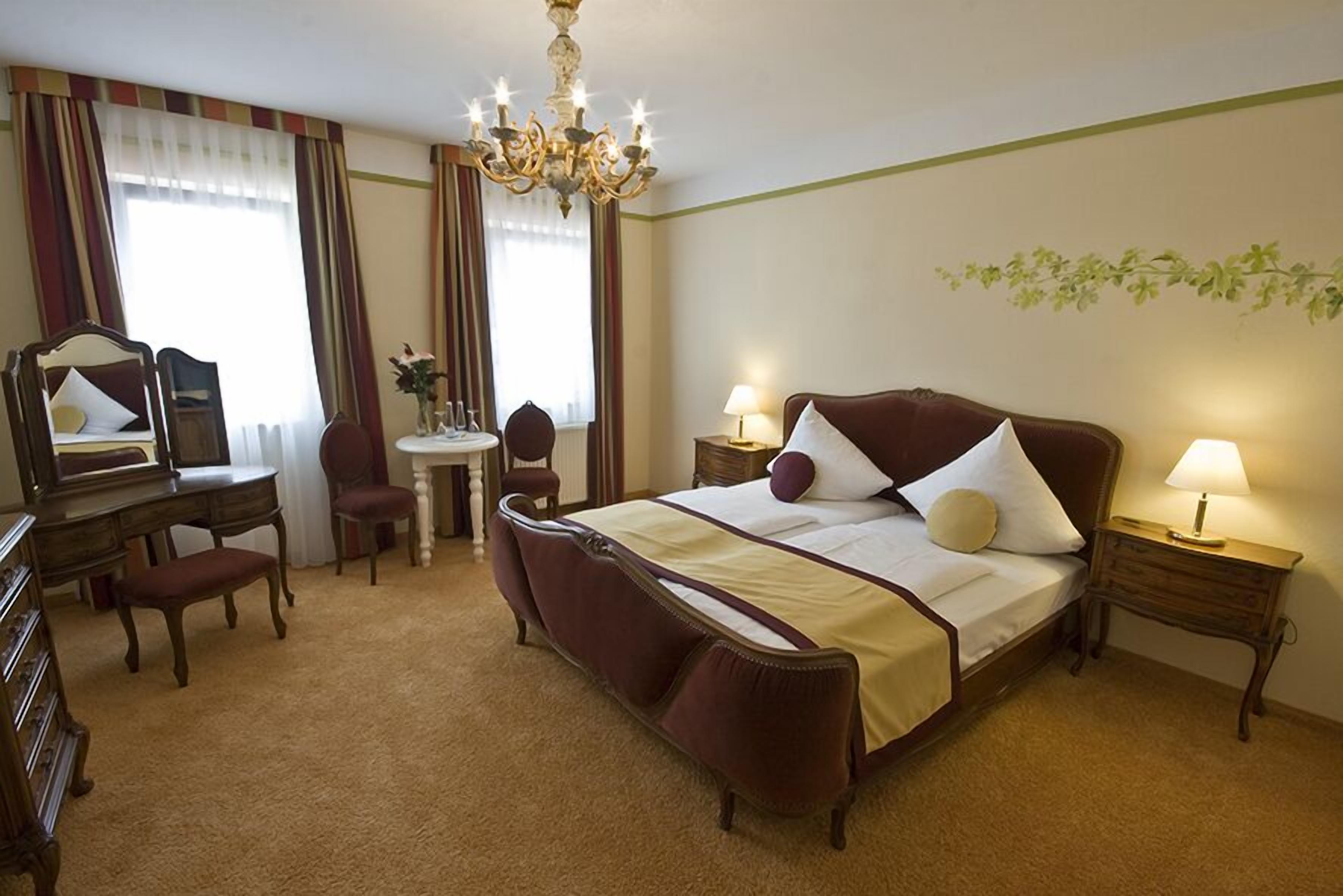 A hotel room with a large bed, a desk with a chair, a mirror, and two bedside tables with lamps.