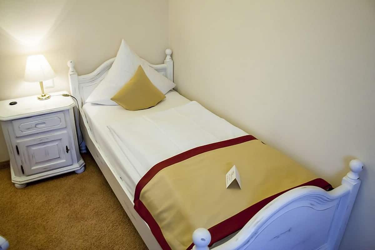 A single bed with a white headboard, a bedside table with a lamp, and a beige throw blanket.