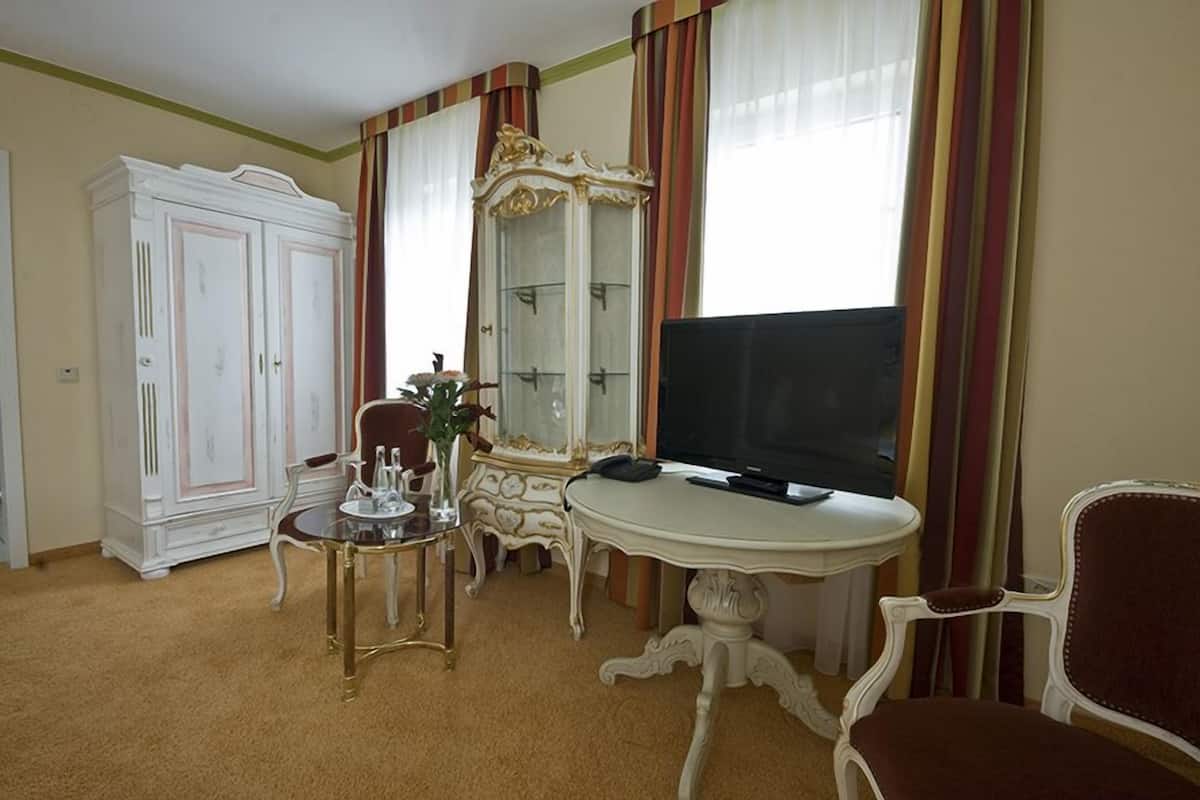 A room with a television, a white cabinet, a mirror, and a small table with a vase.