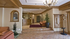 A spacious lobby with a reception desk, a seating area with a sofa and armchairs, a large potted plant, and a chandelier. - Hotel Restaurant Speeter (Weisenheim am Berg)