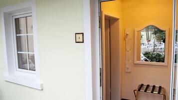 Una habitación con pared blanca, ventana, puerta con espejo y un pequeño banco.