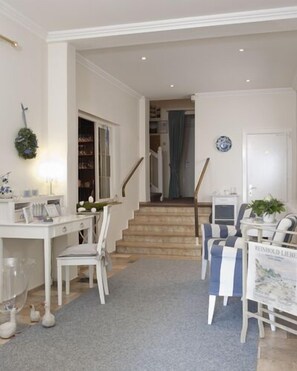 A spacious living area with a staircase leading to a second floor, a white desk with chairs, a dining table with striped chairs, and a bookshelf. - Hotel Parkfrieden (Timmendorfer Strand)