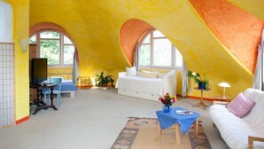 Ein geräumiges Dachzimmer mit hohen Decken, einem weißen Sofa, einem blauen Tisch und einem Bett mit weißem Baldachin.
