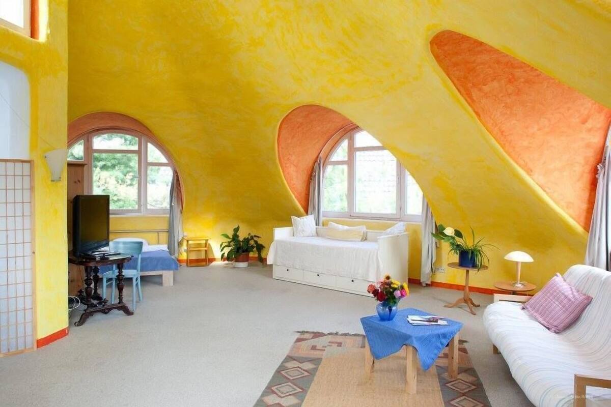 A spacious attic room with high ceilings, a white sofa, a blue table, and a bed with a white canopy.