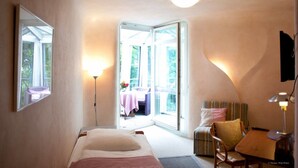 Ein Hotelzimmer mit einem Bett, einem Schreibtisch mit Stuhl, einem Tisch mit Stuhl, einer Stehlampe und einem großen Fenster mit Blick ins Freie.