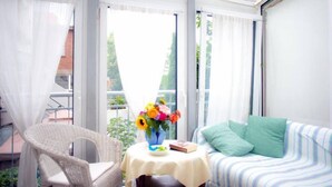 Ein sonnendurchflutetes Zimmer mit einem Korbsessel, einem gestreiften Sofa und einem Tisch mit Blumen in einer Vase.