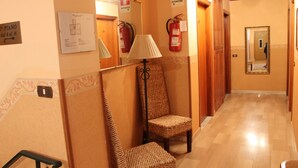 Un pasillo con piso de madera, una silla de mimbre, una lámpara y un extintor en la pared.