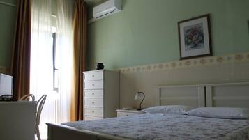 Un dormitorio con cama, cómoda, escritorio con computadora y ventana con cortinas.