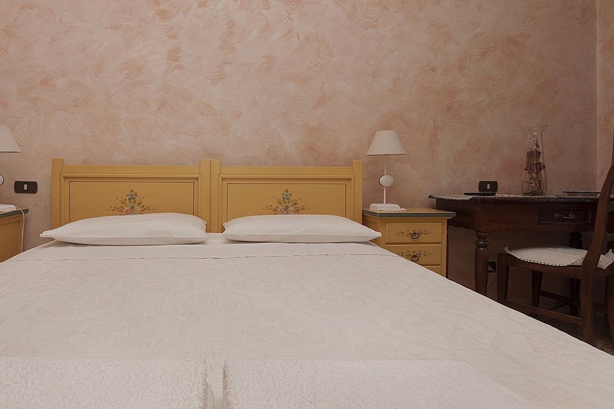 Habitación de hotel con cama doble, dos mesitas de noche con lámparas, una silla de madera y un escritorio con silla.