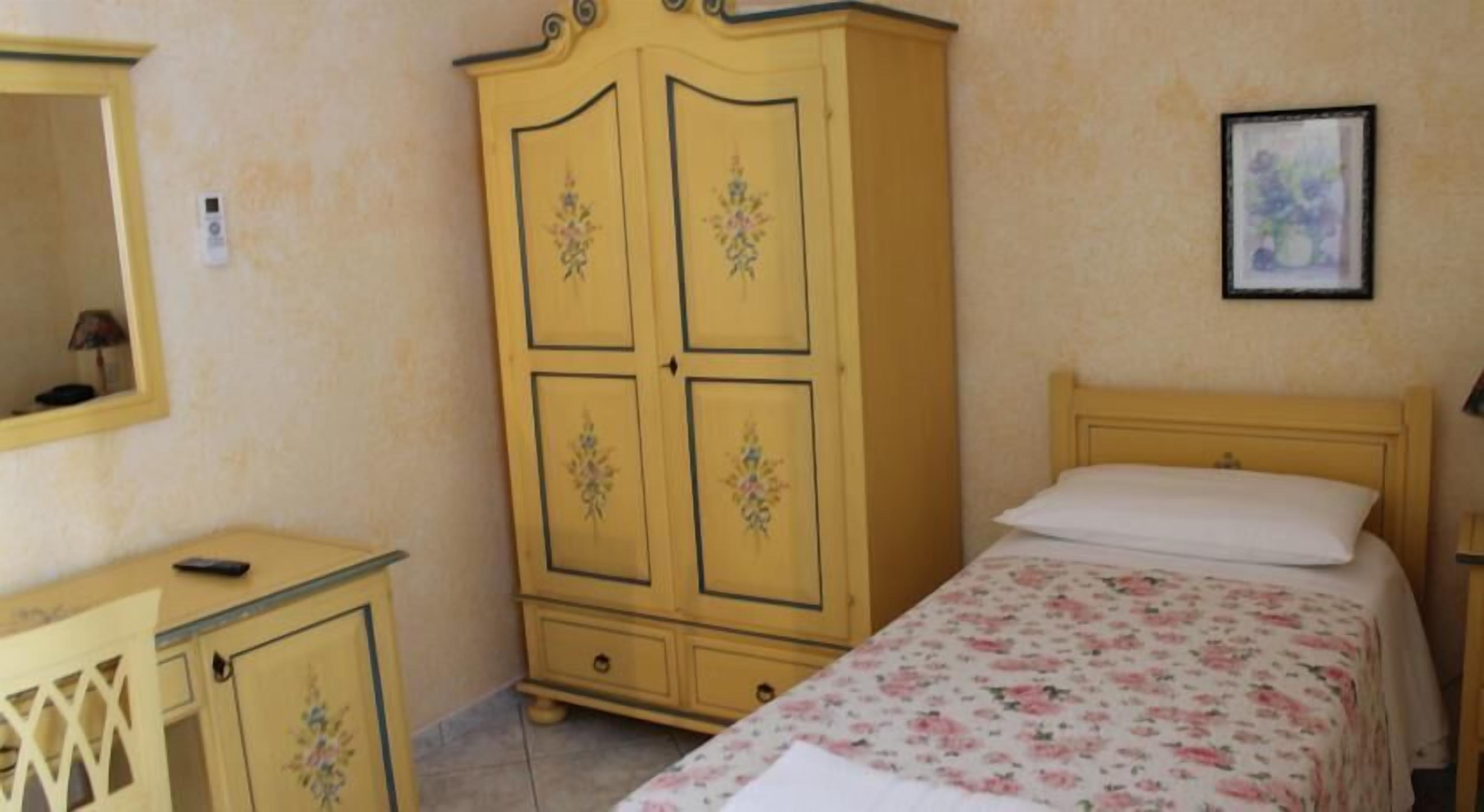 A bedroom with a bed, a wooden wardrobe, a bedside table, and a framed picture on the wall.