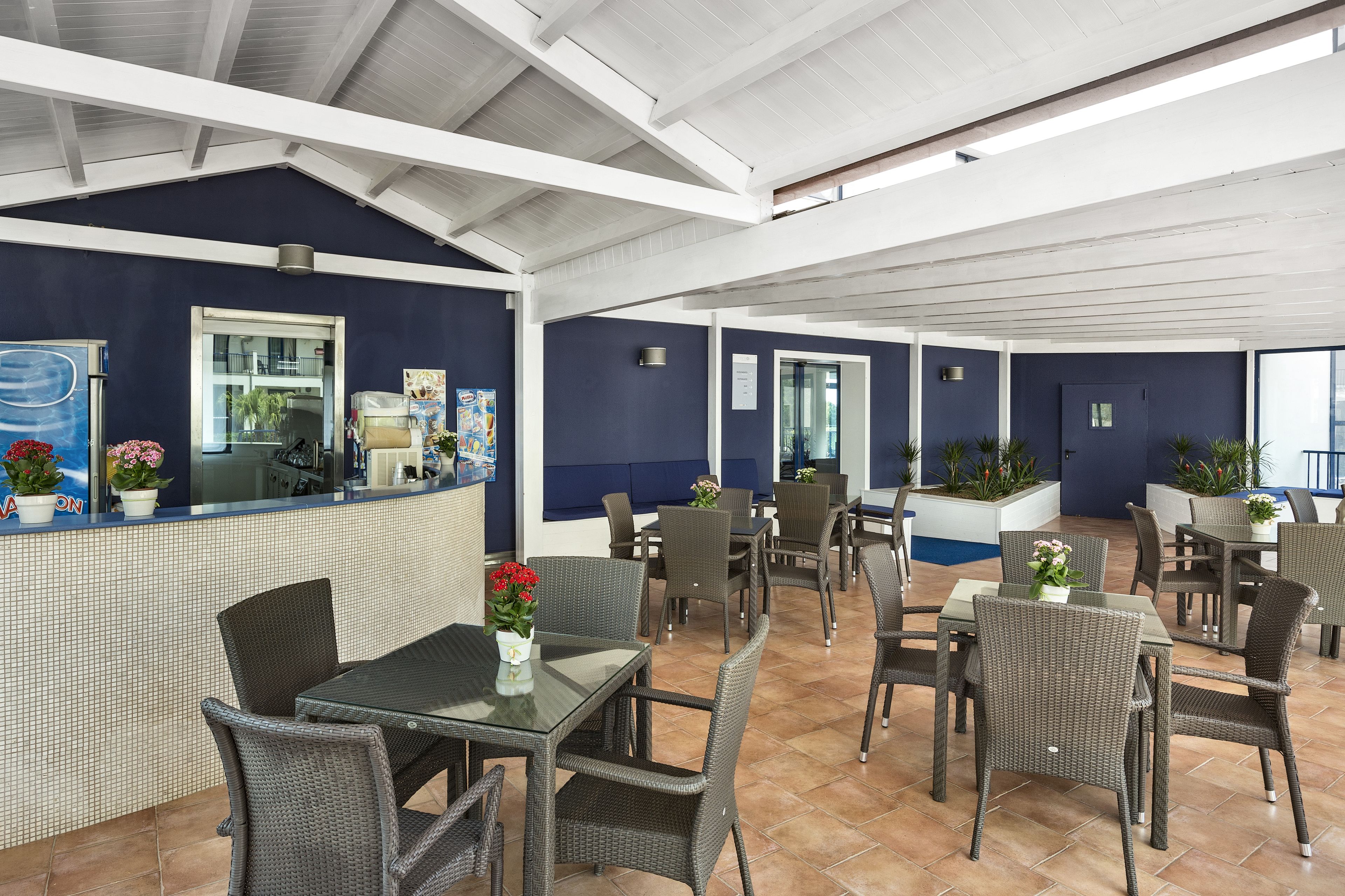 Un patio interior con mobiliario de mimbre, una barra con menú y plantas en macetas.