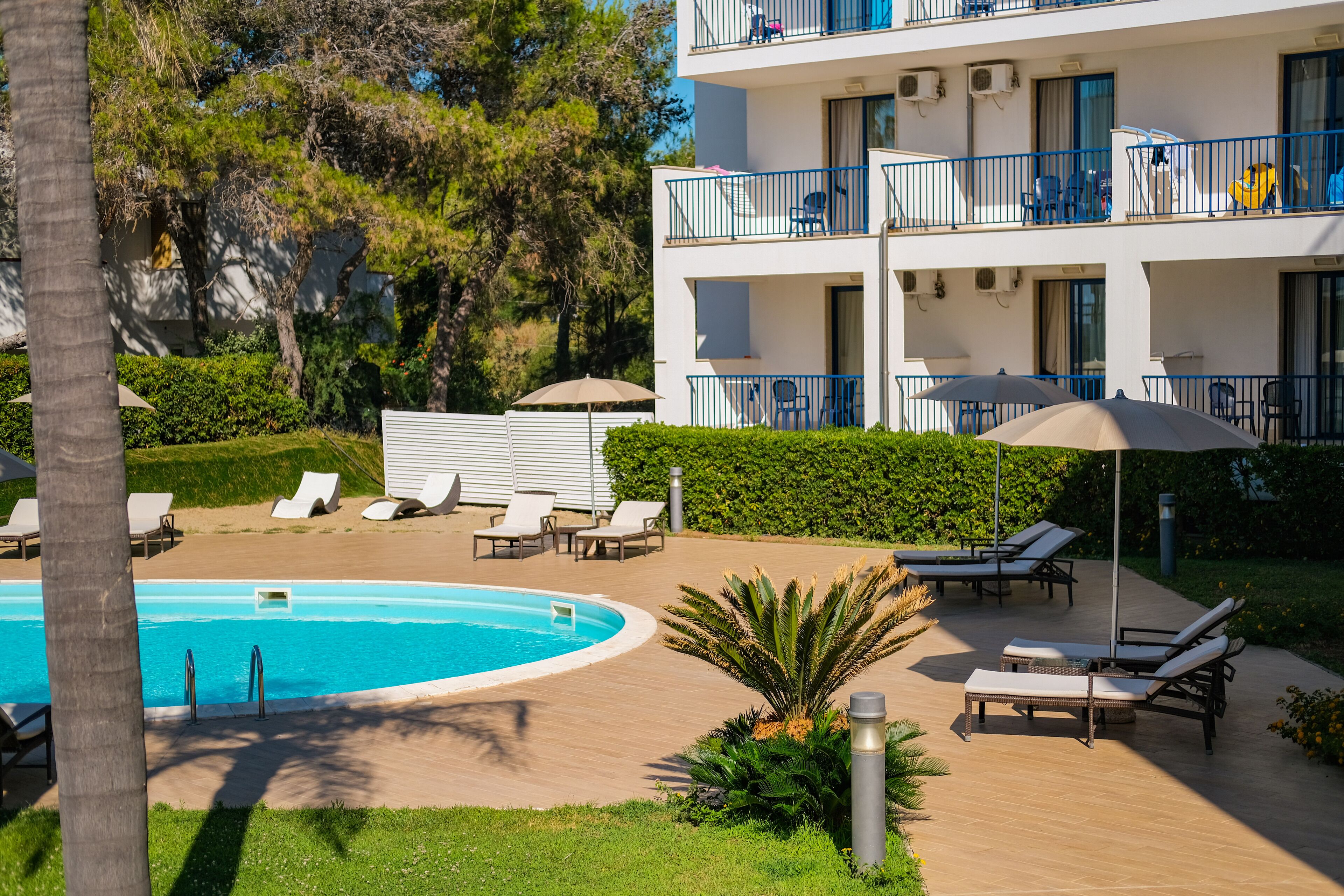 A poolside area with lounge chairs, a swimming pool, and a multi-story building with balconies.