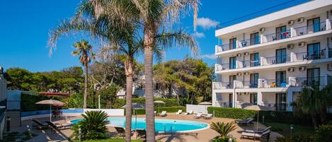 Un hotel con piscina, sillas de descanso al aire libre y palmeras.