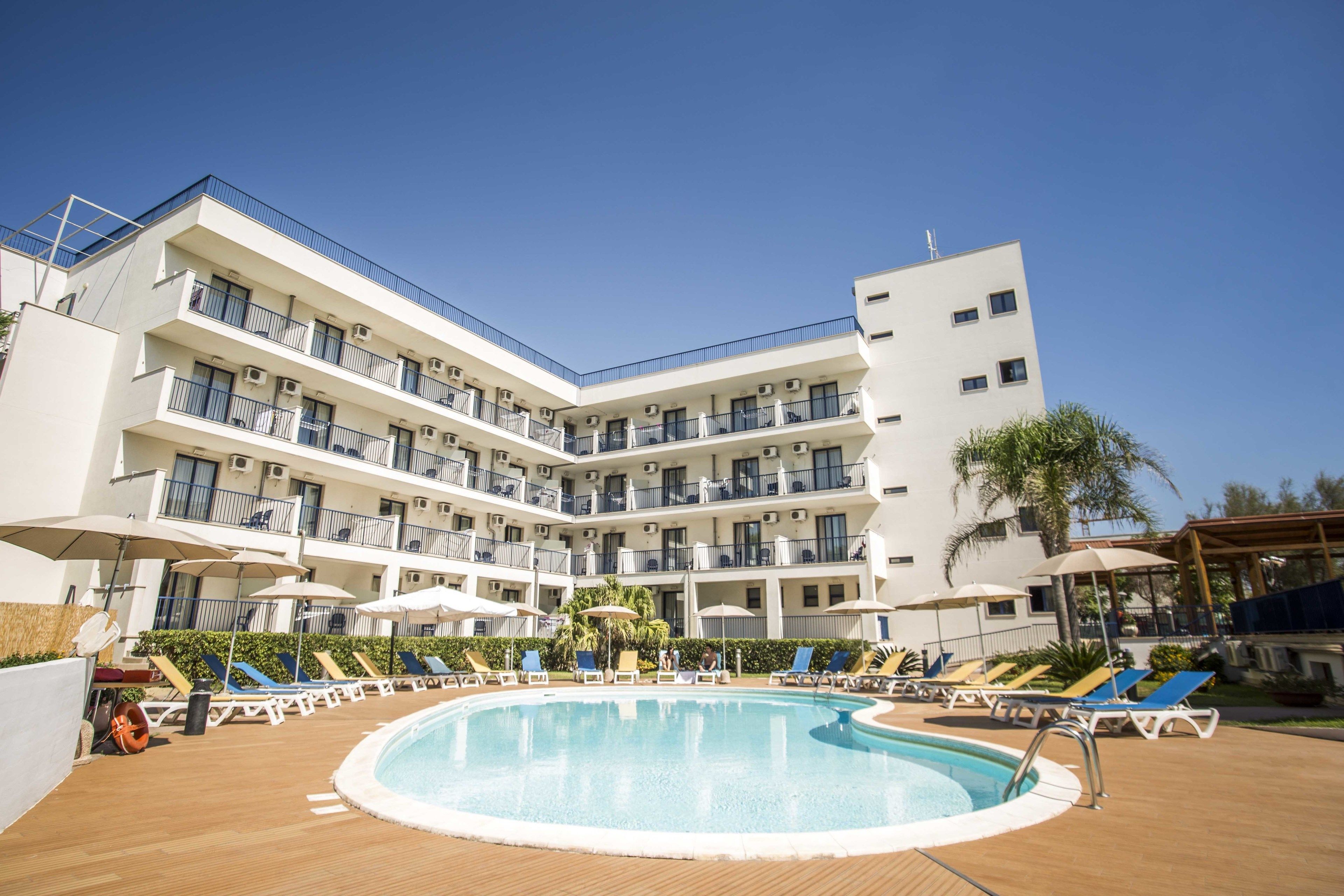 Een meerlaags hotel met een zwembad, ligbedden en parasols.