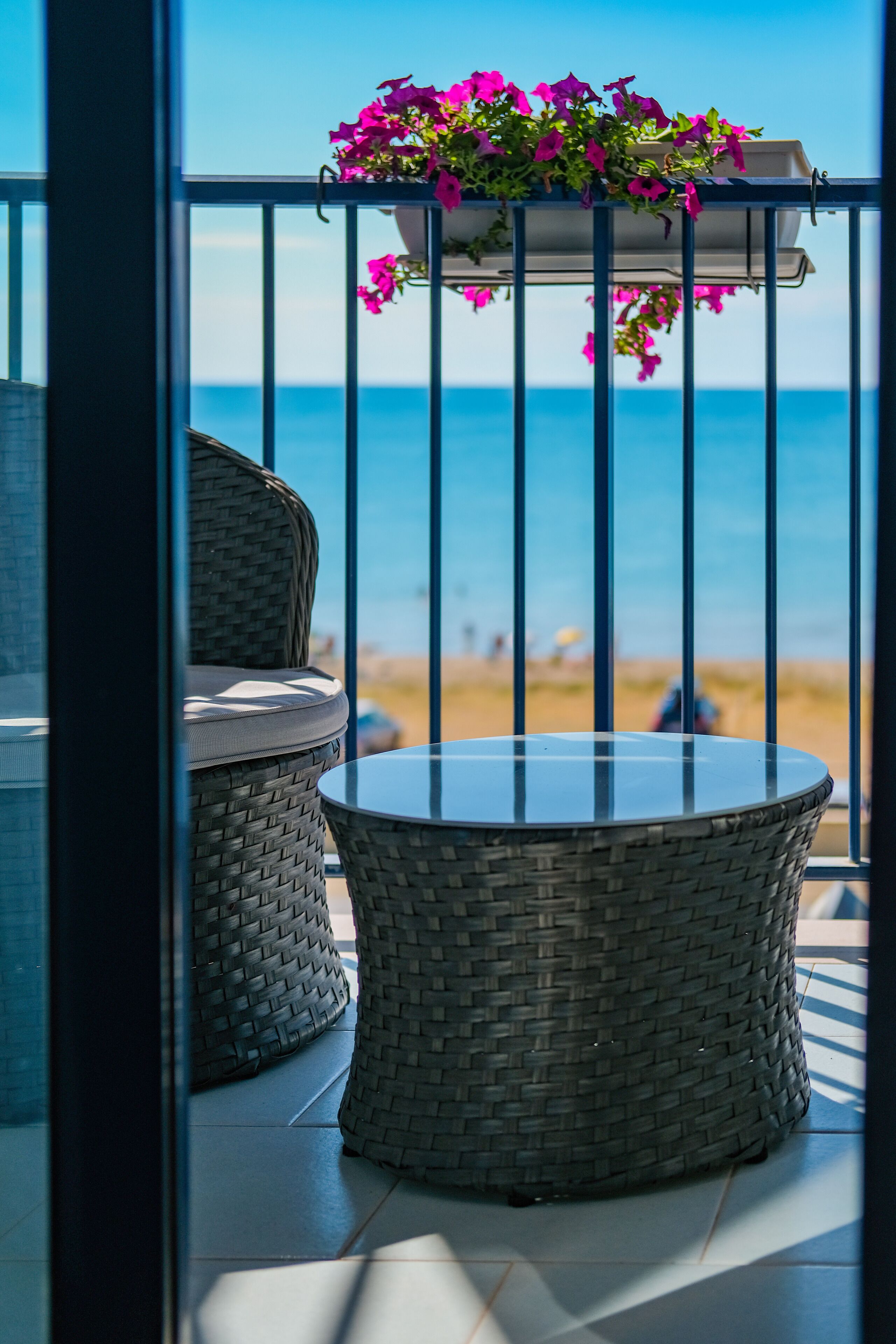 Un balcón con mobiliario de mimbre y una mesa de vidrio, con vista a la playa.