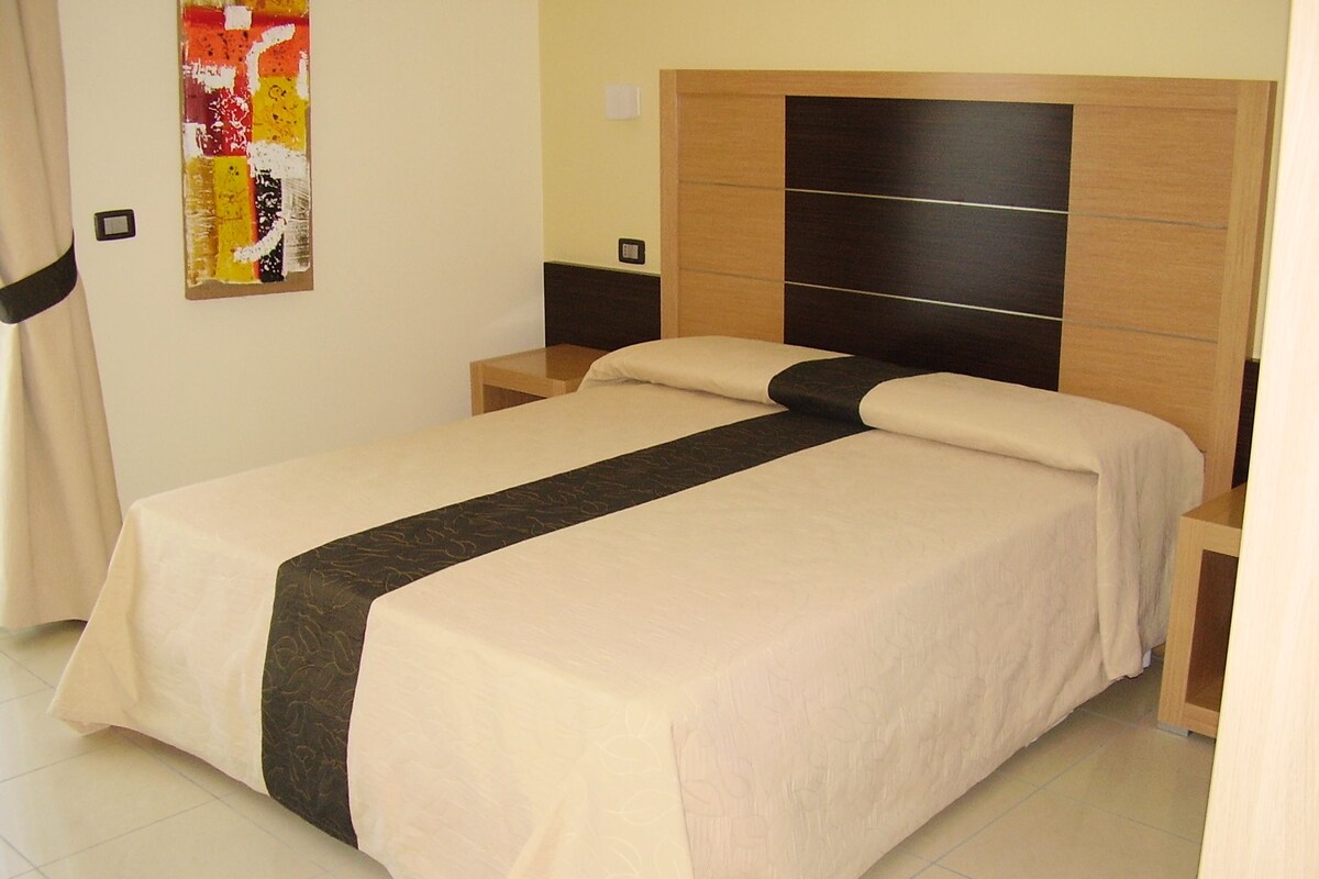 A neatly made bed with a white and dark-colored bedspread, wooden headboard, and bedside tables.