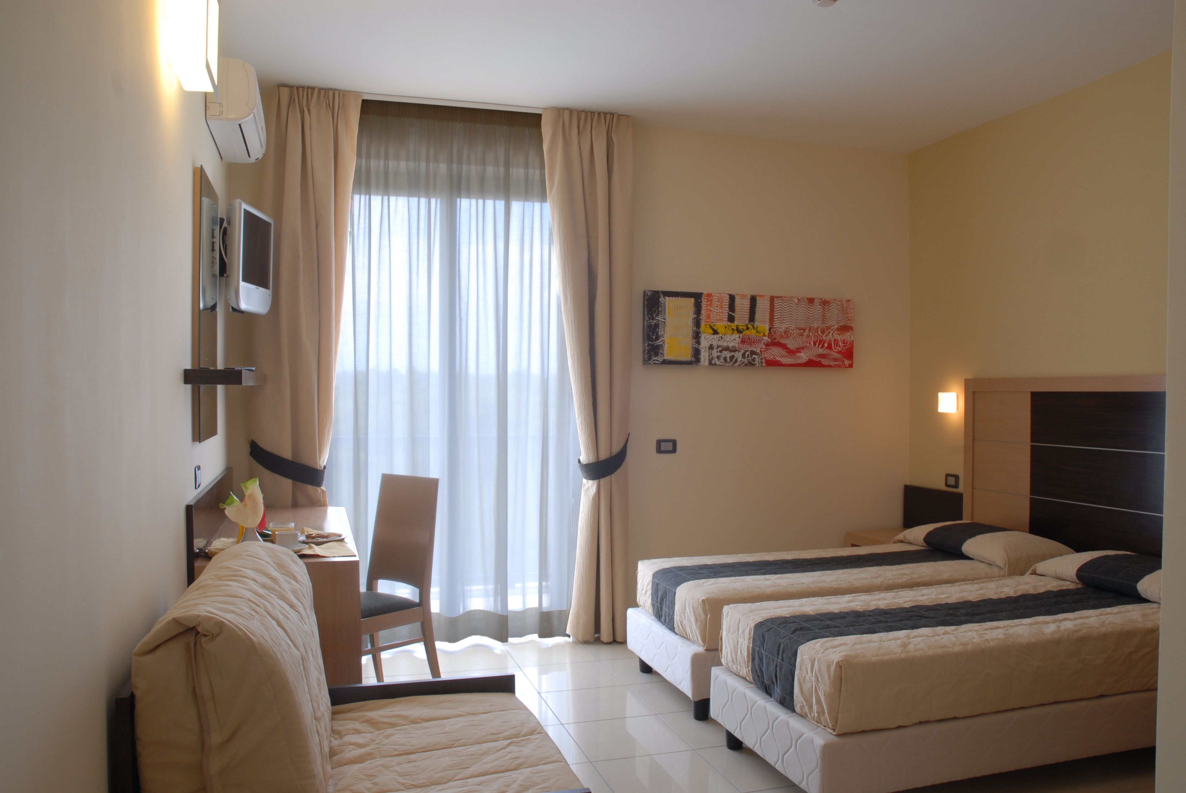 Habitació d'hotel amb dos llits, un escriptori, una cadira i una finestra gran amb cortines.