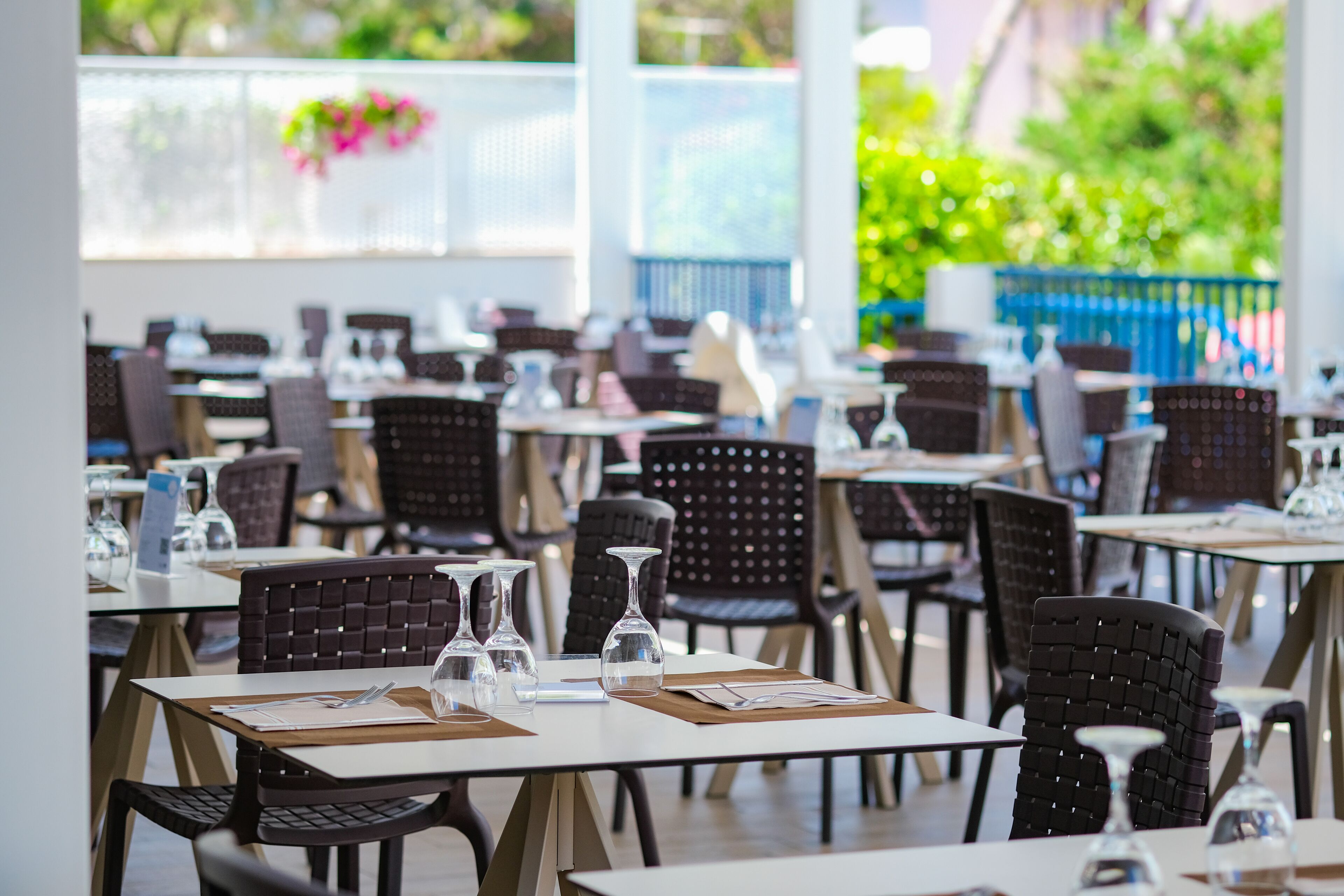 A restaurant with multiple tables and chairs, each set with wine glasses and menus.