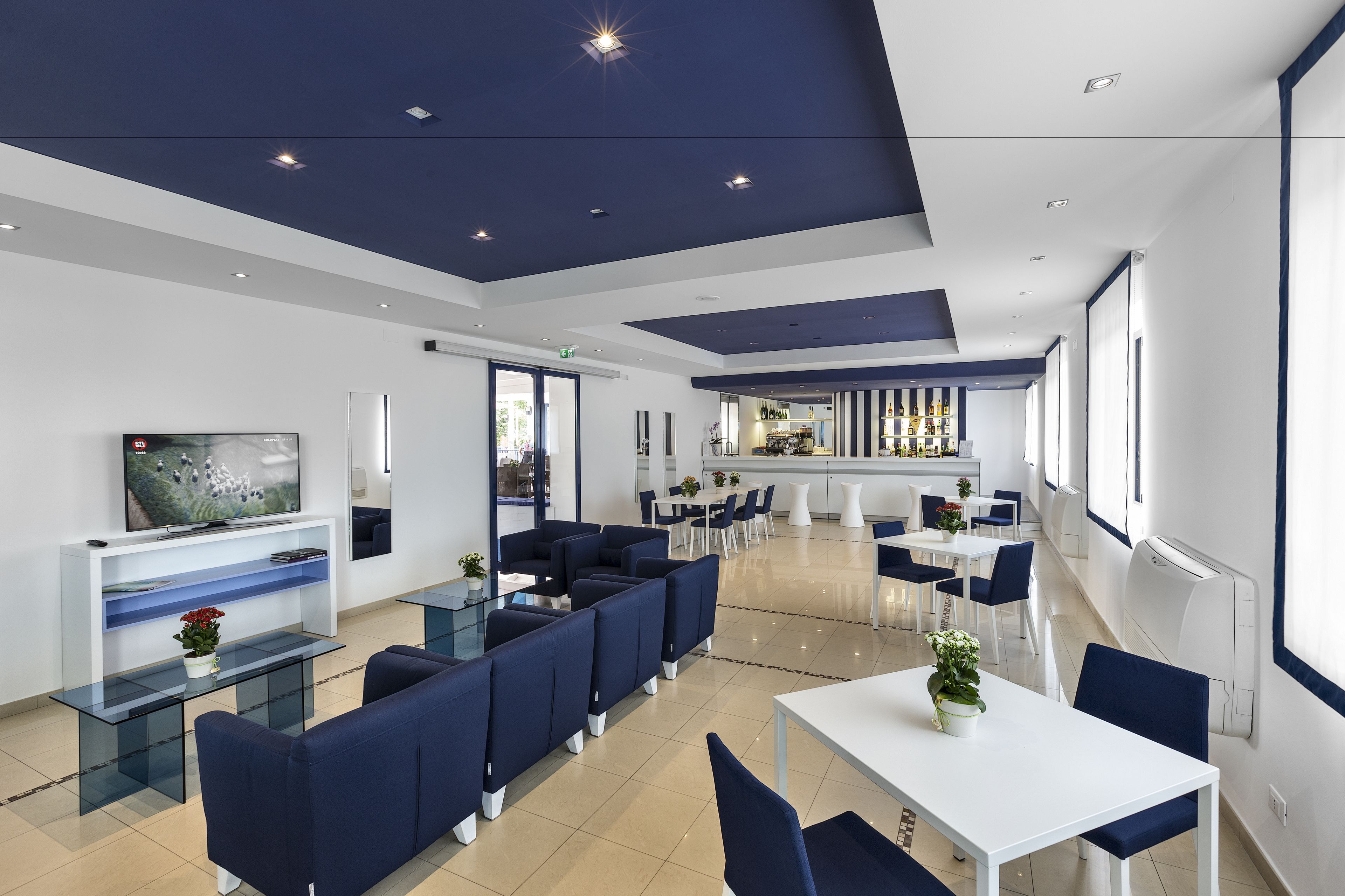 Un hall d’hôtel moderne doté d’un bar, d’espaces aménagés avec des sièges et d’un téléviseur.