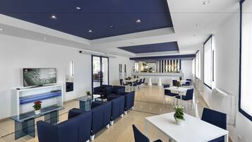 Un hall d’hôtel moderne doté d’un bar, d’espaces aménagés avec des sièges et d’un téléviseur.