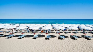 Une plage bordée de rangées de chaises longues et de parasols, un ciel bleu azur et l’océan en toile de fond.