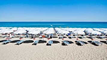 Een privéstrand, ligstoelen aan het strand, parasols, een strandbar