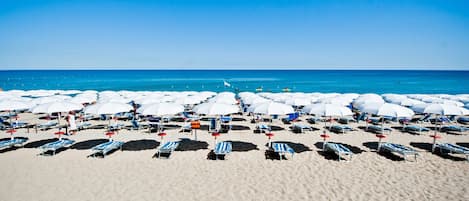 Een privéstrand, ligstoelen aan het strand, parasols, een strandbar