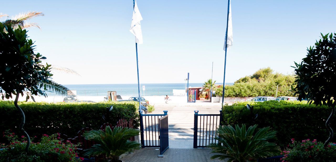 A pathway leading to a beach with a gate, surrounded by greenery and a clear view of the ocean.