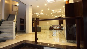 A modern hotel lobby with a marble staircase, a reception desk, and a glass partition. - Hotel Dayal (Udaipur)