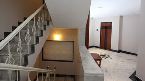 A staircase with ornate railings leading to a landing with a light fixture. A wooden door is visible in the background. - Hotel Dayal (Udaipur)