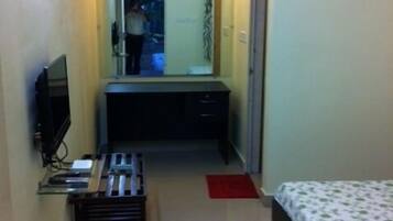 A narrow hallway leading to a bedroom with a bed, a desk, and a television.