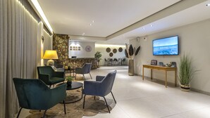 A modern hotel lobby with a seating area, a TV, and a stone wall.