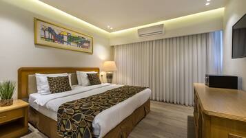 A modern hotel room with a large bed, a flat-screen TV, a bedside table, a lamp, and a painting on the wall.