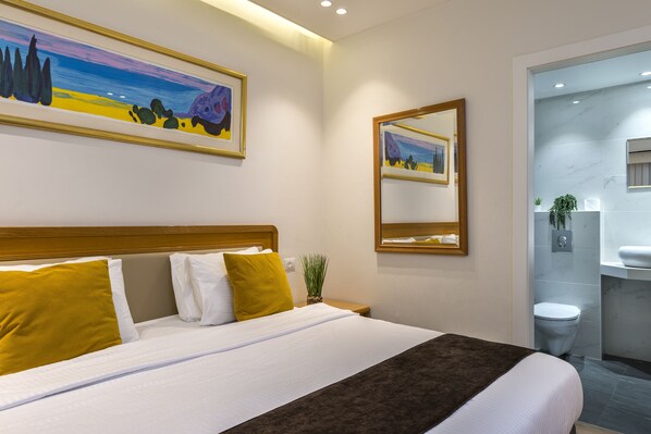 A hotel room with a bed, a nightstand, a mirror, and a bathroom visible through an open door. - Melio Hotel Eilat (Eilat)