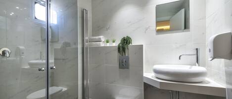 Un baño moderno con ducha de mampara de vidrio, inodoro blanco y zona de lavamanos con mosaicos de mármol.