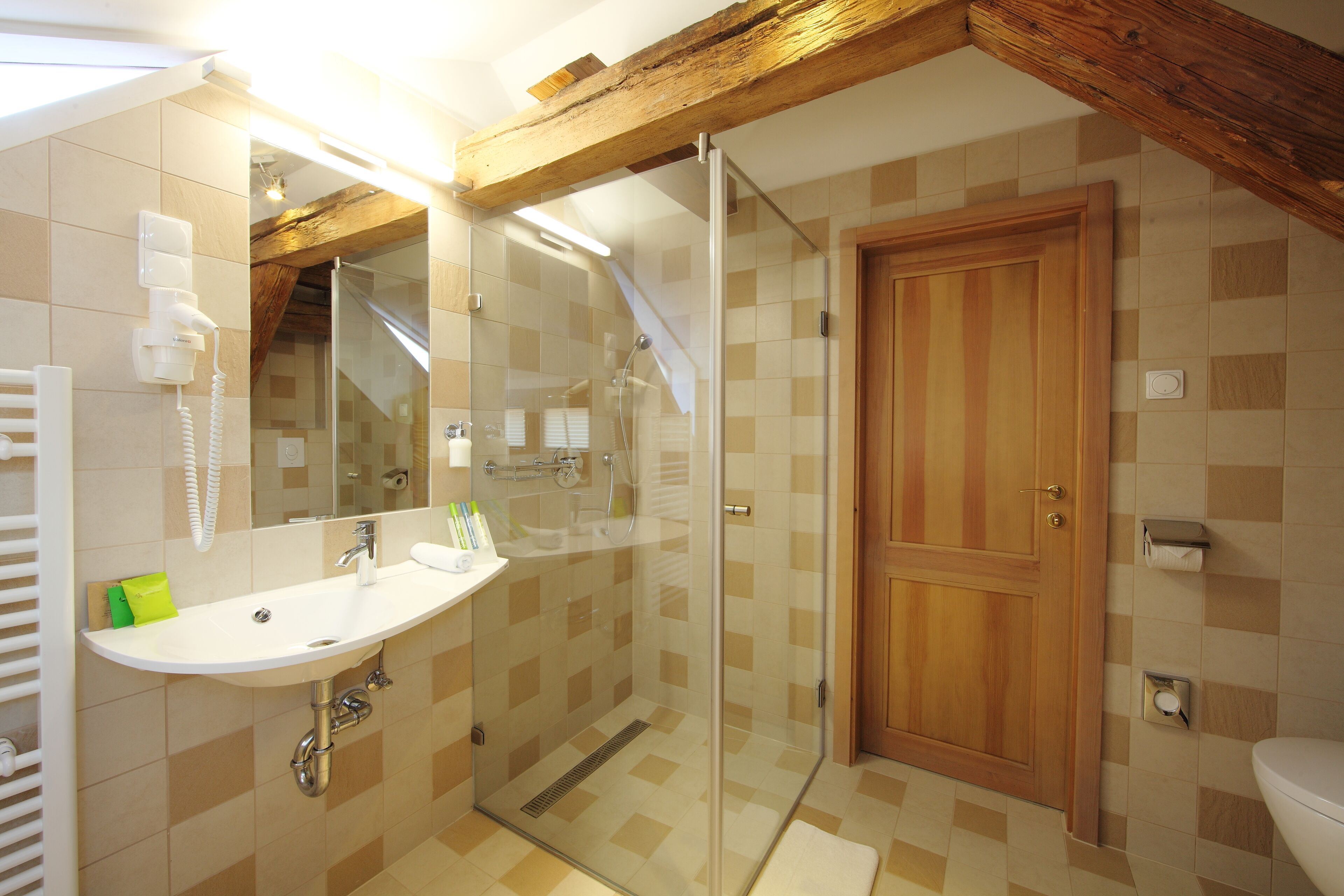 Un baño con ducha de vidrio, un lavamanos blanco y una puerta de madera.