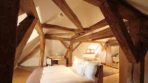 Un dormitorio con techo inclinado y vigas de madera a la vista, una cama, mesitas de noche y un escritorio.