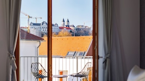 Habitación de hotel con balcón, una cama, dos sillas y vistas a edificios y grúas de construcción.