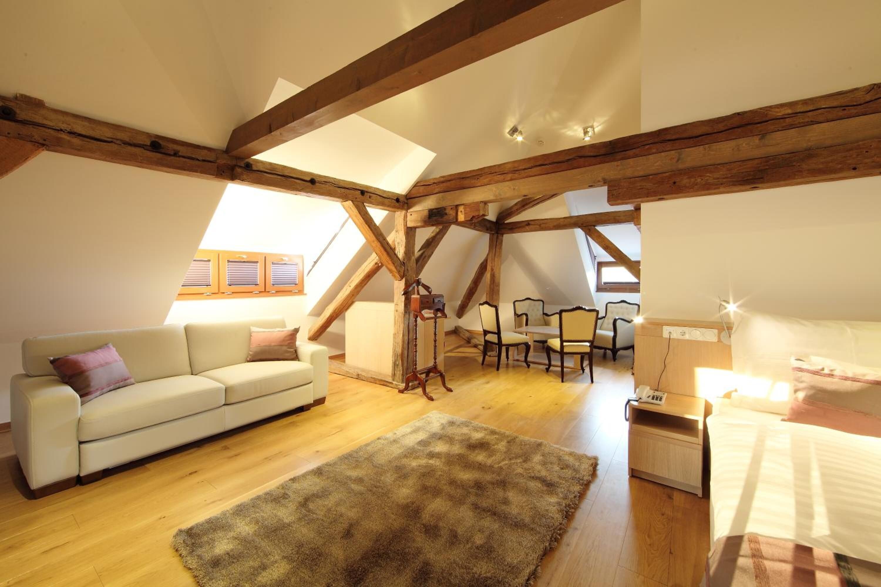 A cozy loft bedroom with a wooden ceiling, a white bed, a nightstand, a fluffy rug, and a sofa with pillows.