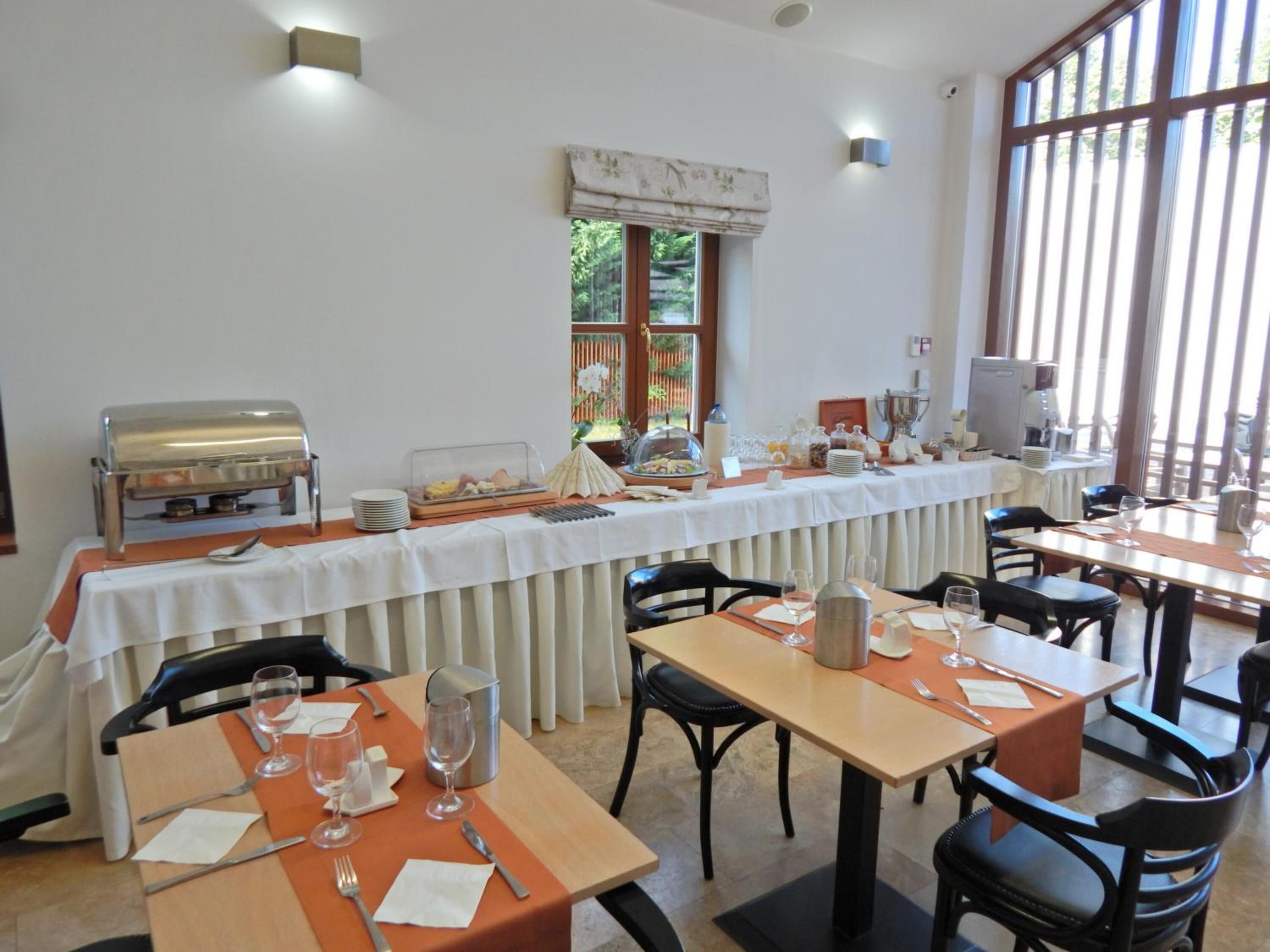 A dining area with tables set for breakfast, a buffet with various food items, and a coffee machine.