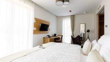 A modern hotel room with a large bed, a desk, a chair, a TV mounted on the wall, and a wardrobe.