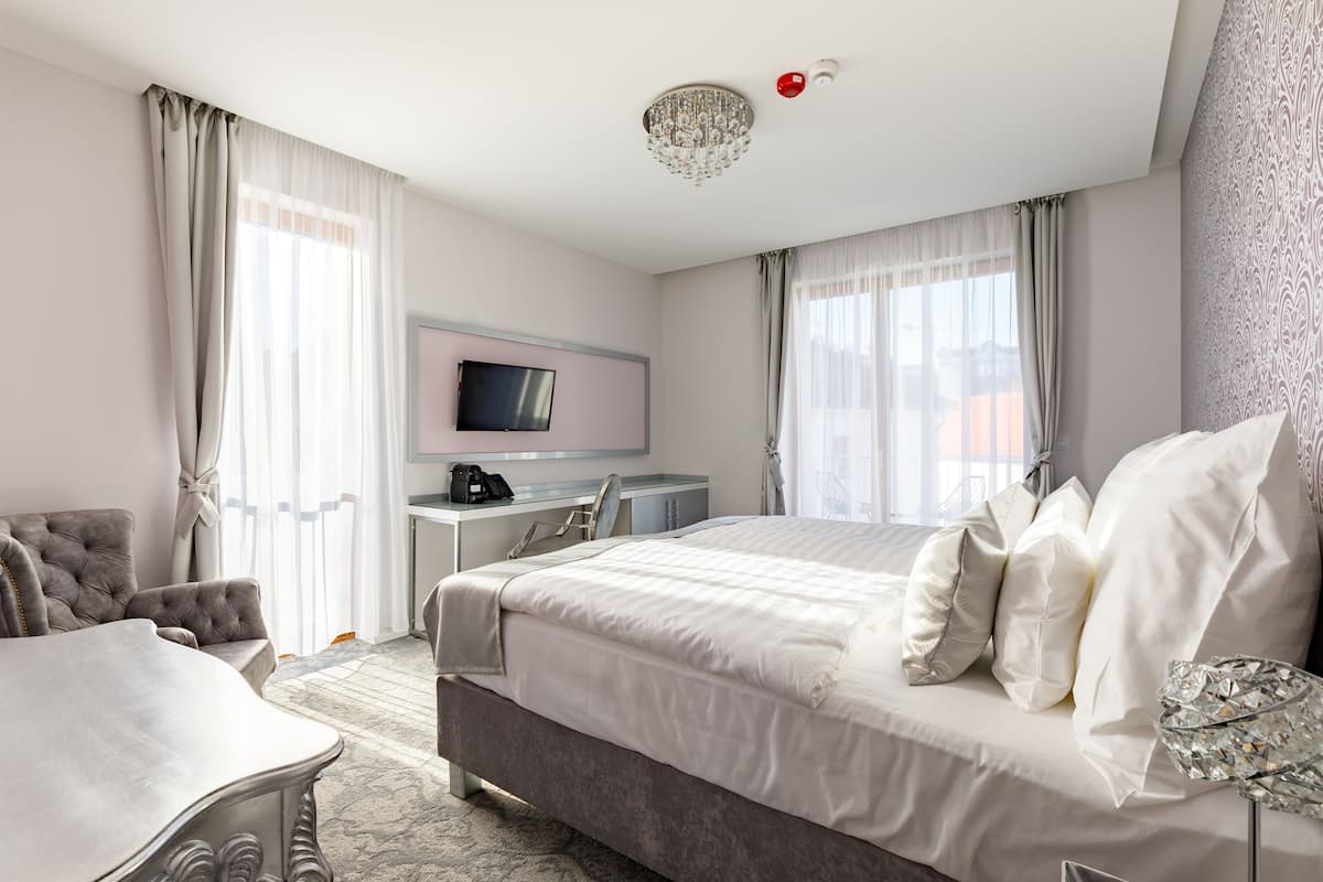 A hotel room with a large bed, a desk, a television, and a chandelier.