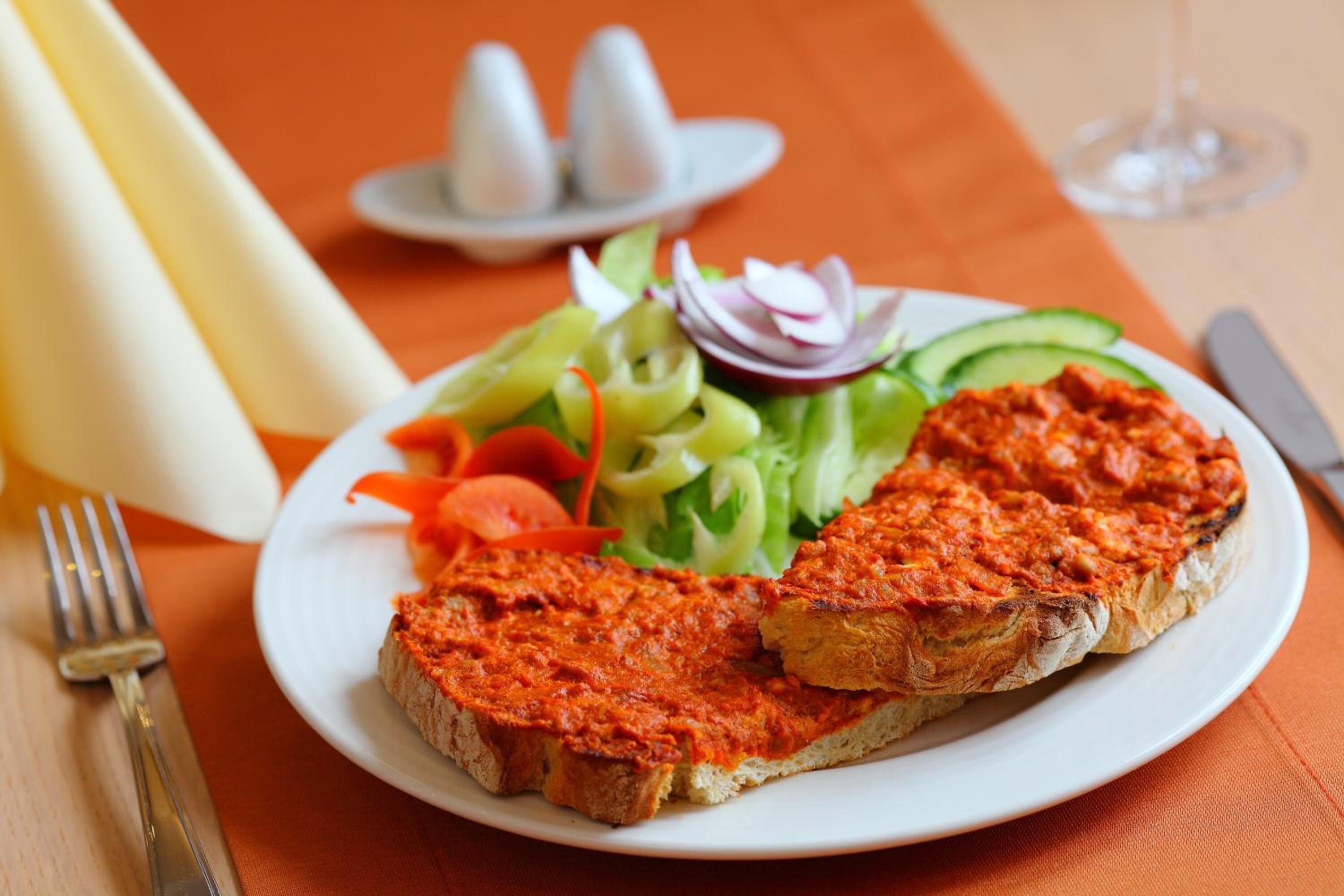 A plate with a slice of toast topped with tomato spread, accompanied by a side salad.
