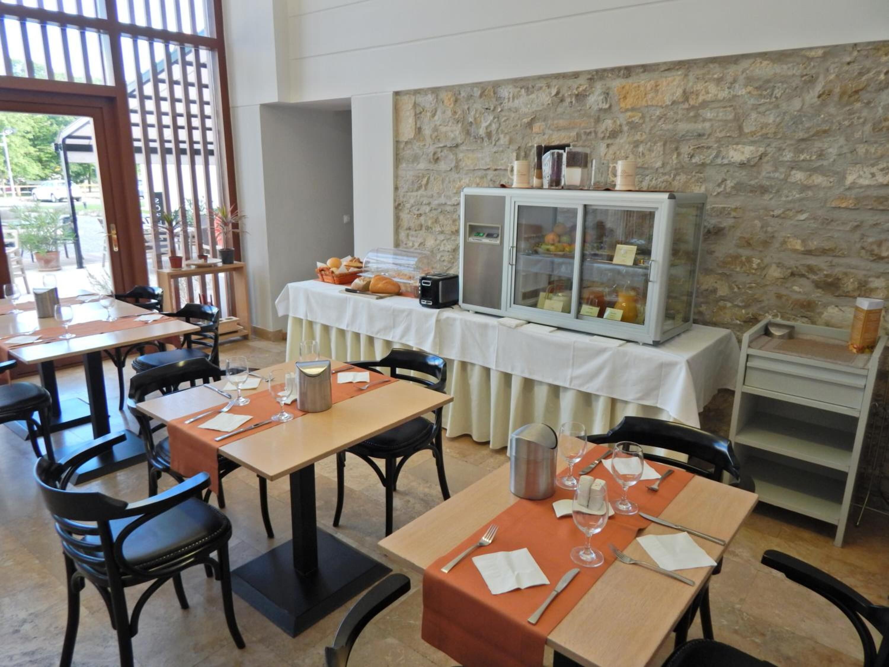 A dining area with tables set for breakfast, a buffet with food and drinks, and a stone wall backdrop.