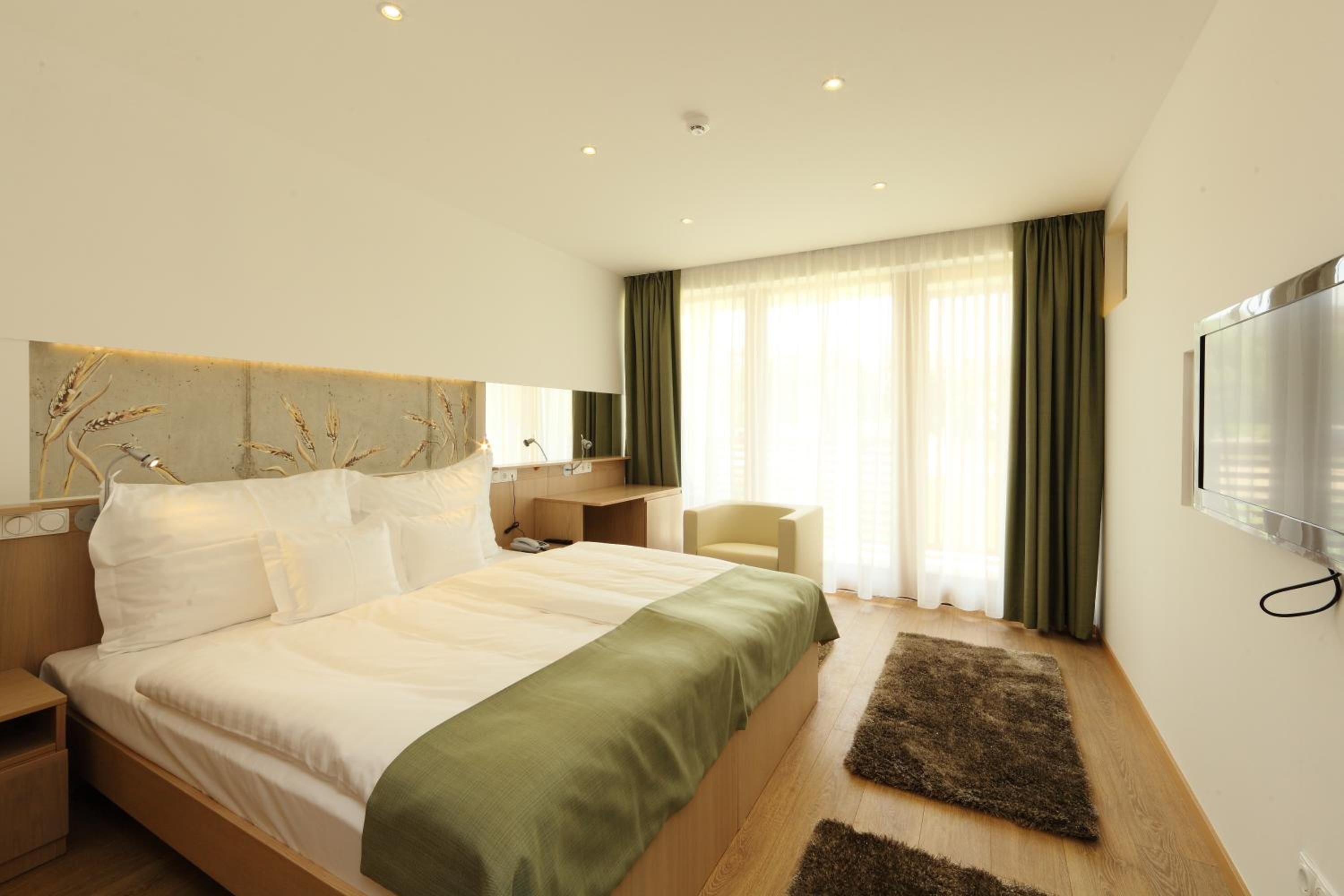 A modern hotel room with a large bed, a desk, a chair, and a TV.