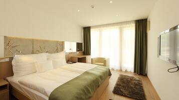 A modern hotel room with a large bed, a desk, a chair, and a TV.