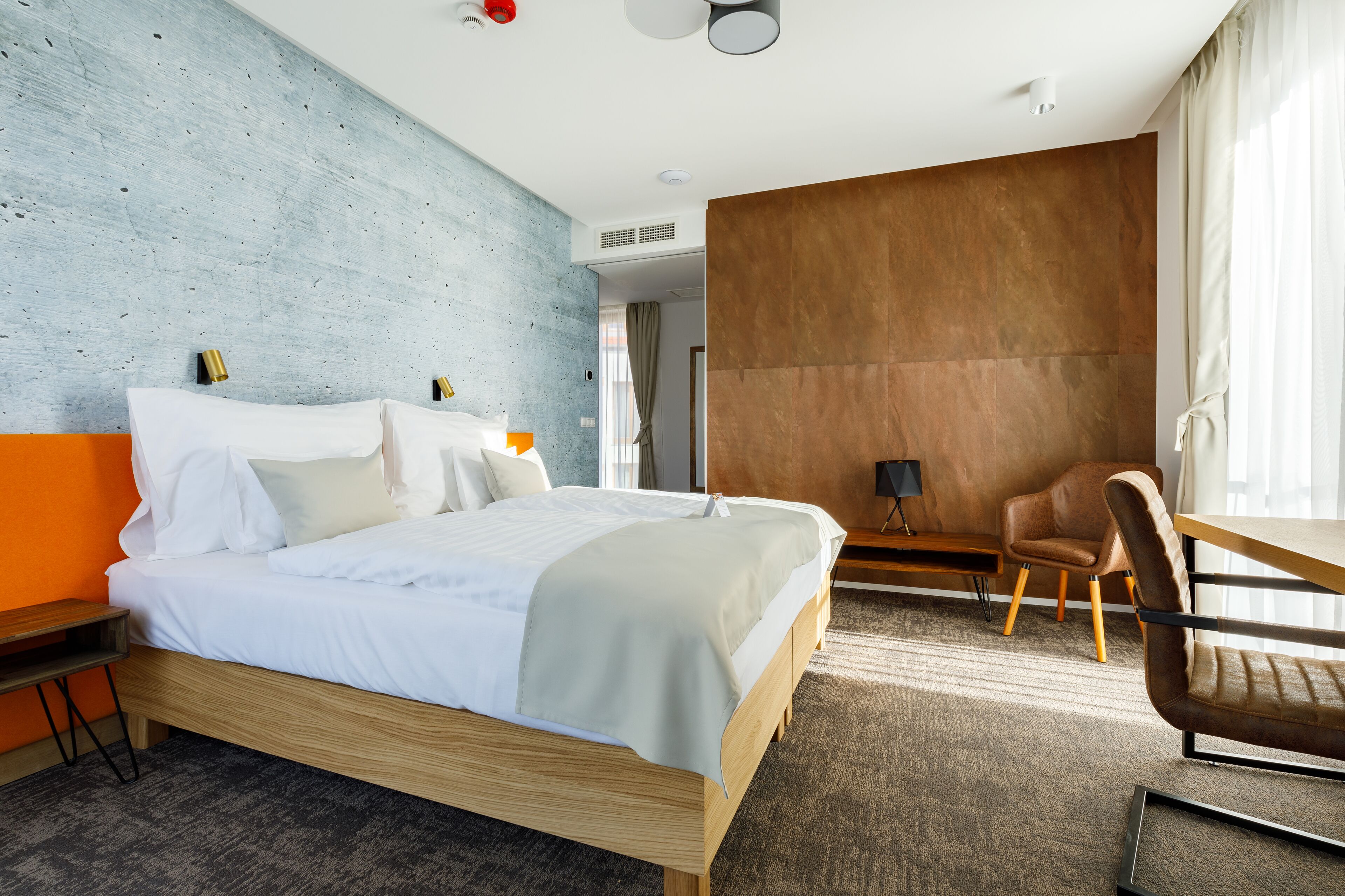 A modern hotel room with a large bed, a wooden desk, and a comfortable chair.