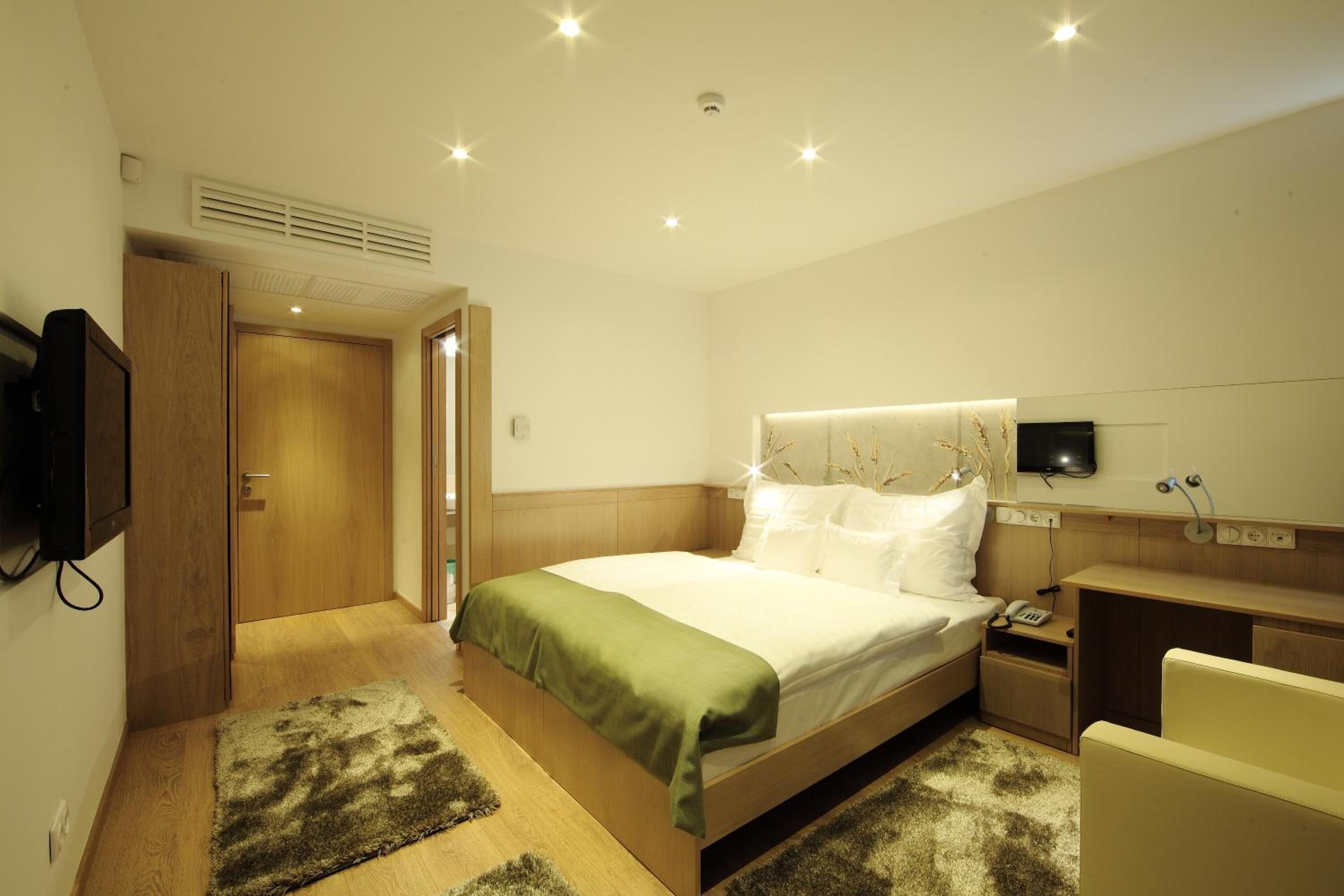 A hotel room with a bed, bedside table, TV, and a desk with a chair.