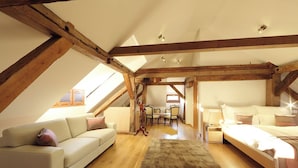 Un dormitorio tipo loft con techo inclinado, vigas de madera, un sofá, una cama y una mesa de comedor.